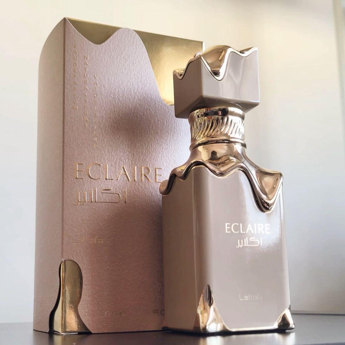 Frasco de perfume, beige y dorado, junto a caja a juego; 