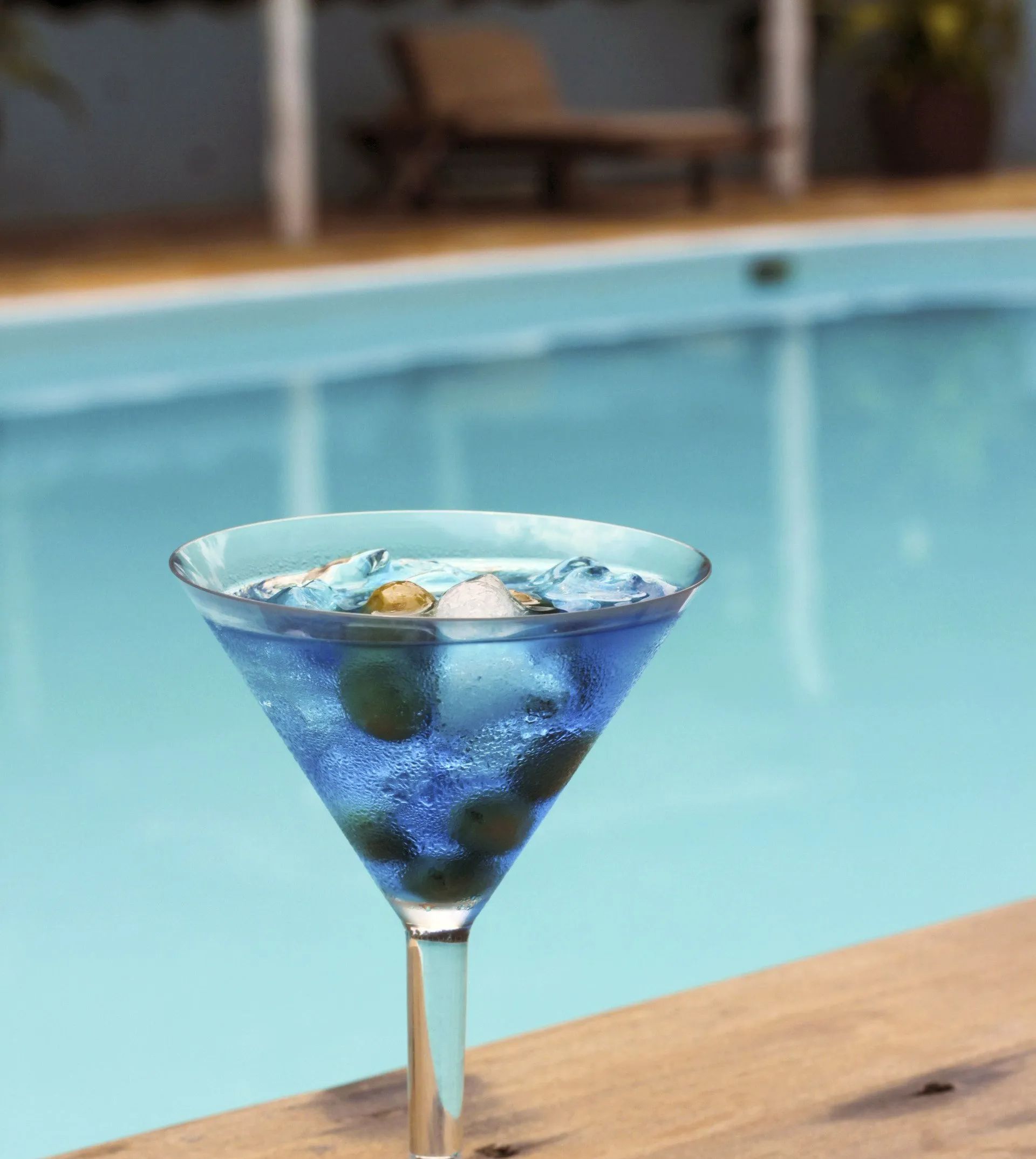 Un verre à martini rempli de liquide bleu et de glace à côté d'une piscine.