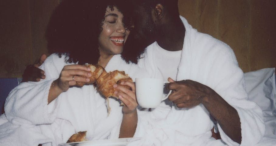Un homme et une femme sont assis dans leur lit en train de manger des croissants et de boire du café.