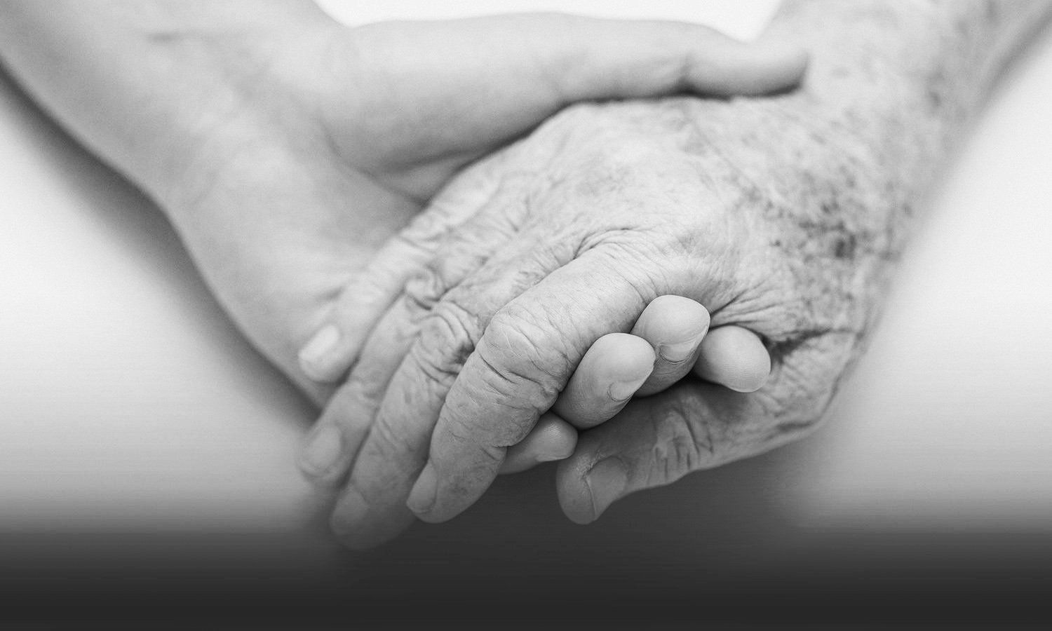 black and white closeup photo of a young person's hand holding elderly person's hand