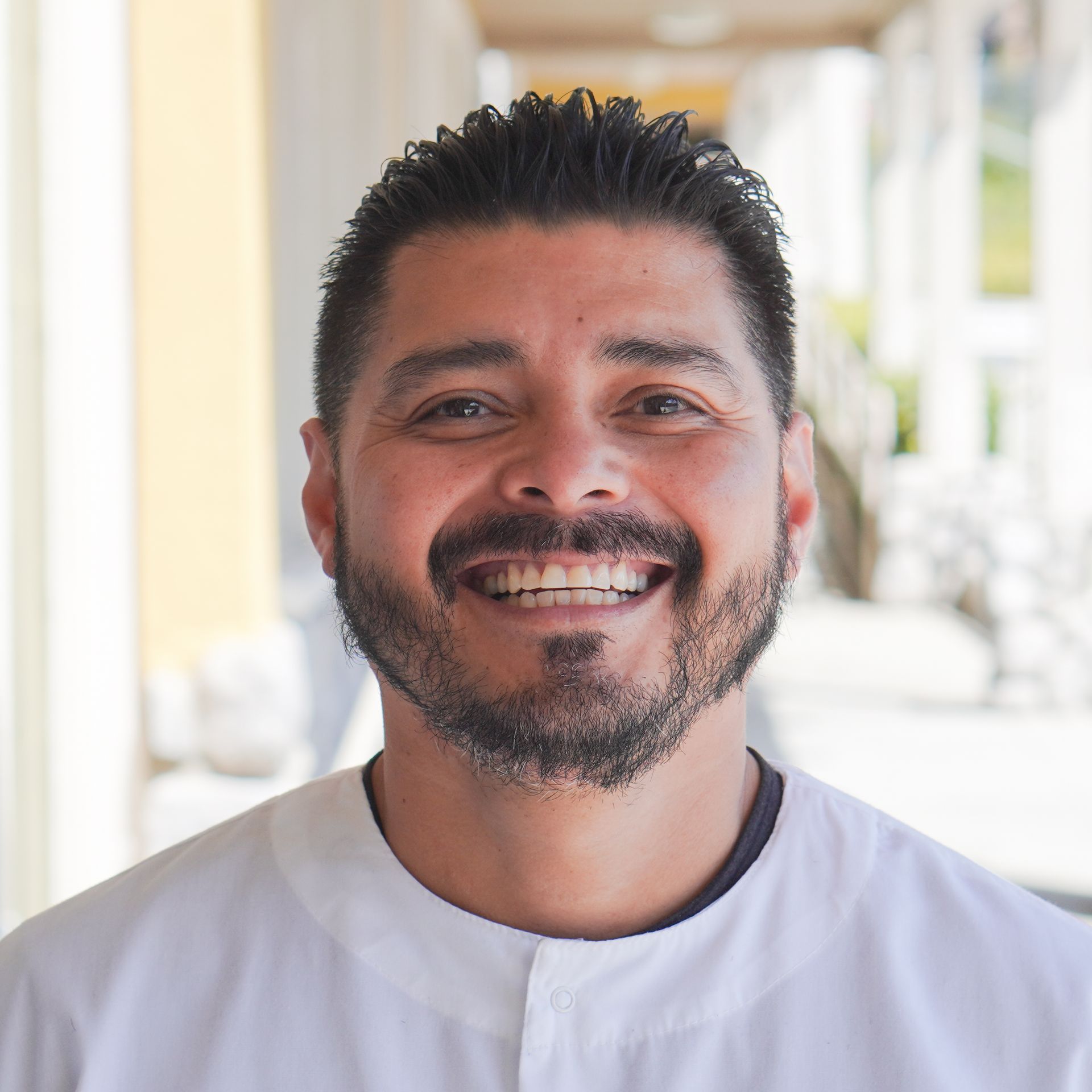 A man with a beard is smiling and wearing a white shirt