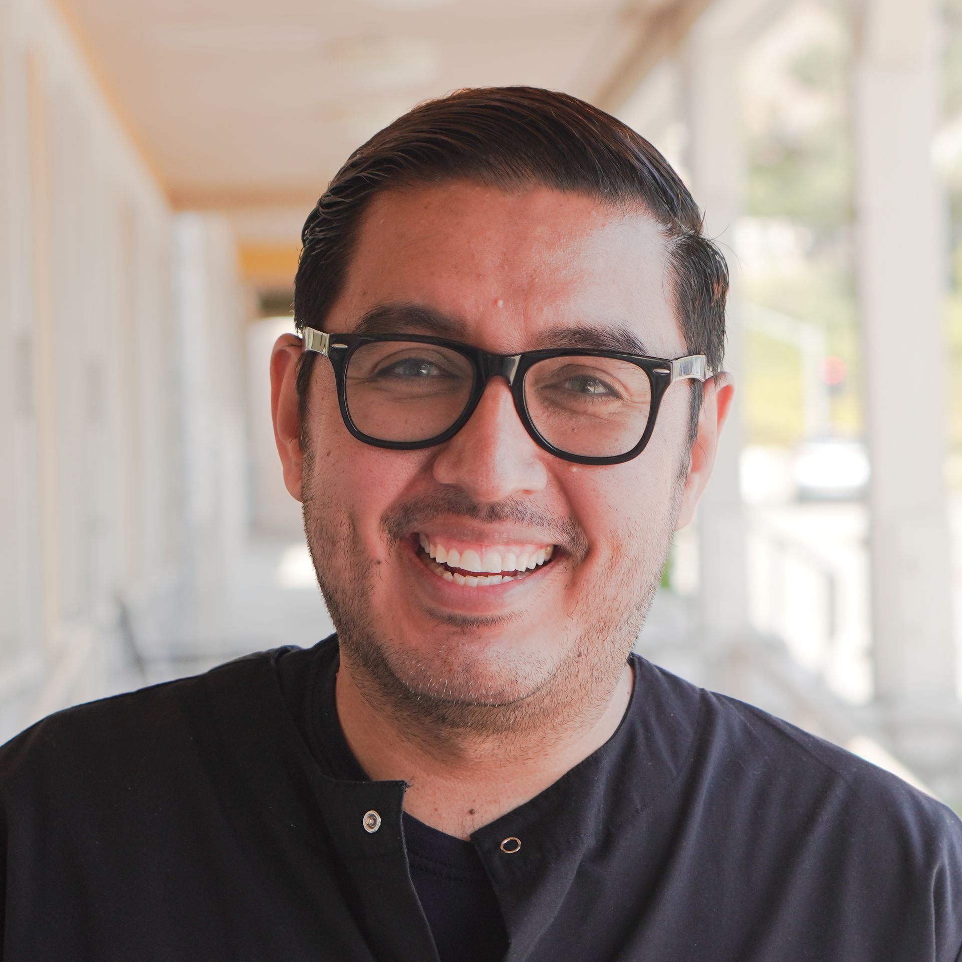 A man wearing glasses and a black shirt is smiling for the camera.