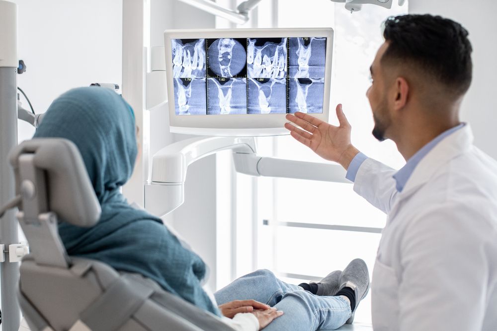 A dentist is talking to a patient who is sitting in a dental chair.