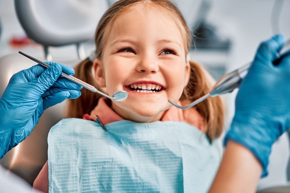 A little girl is sitting in a dental chair while a dentist examines her teeth.