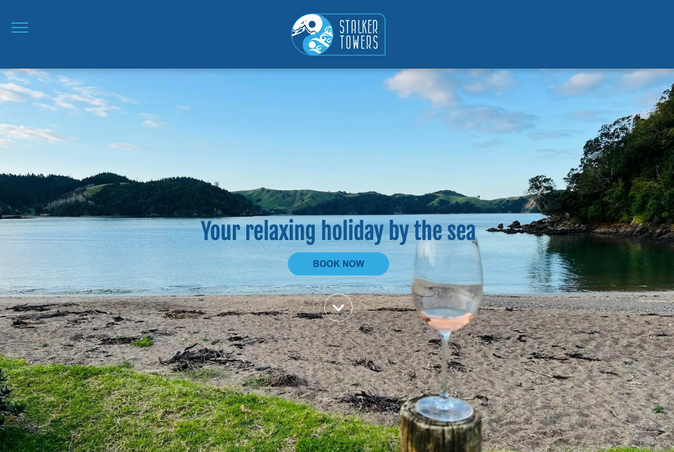 A glass of wine is sitting on the beach next to a body of water.