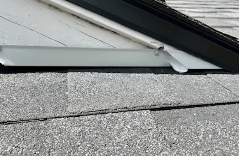 White gutter attached to a roof with gray shingles. Black trim above the gutter.
