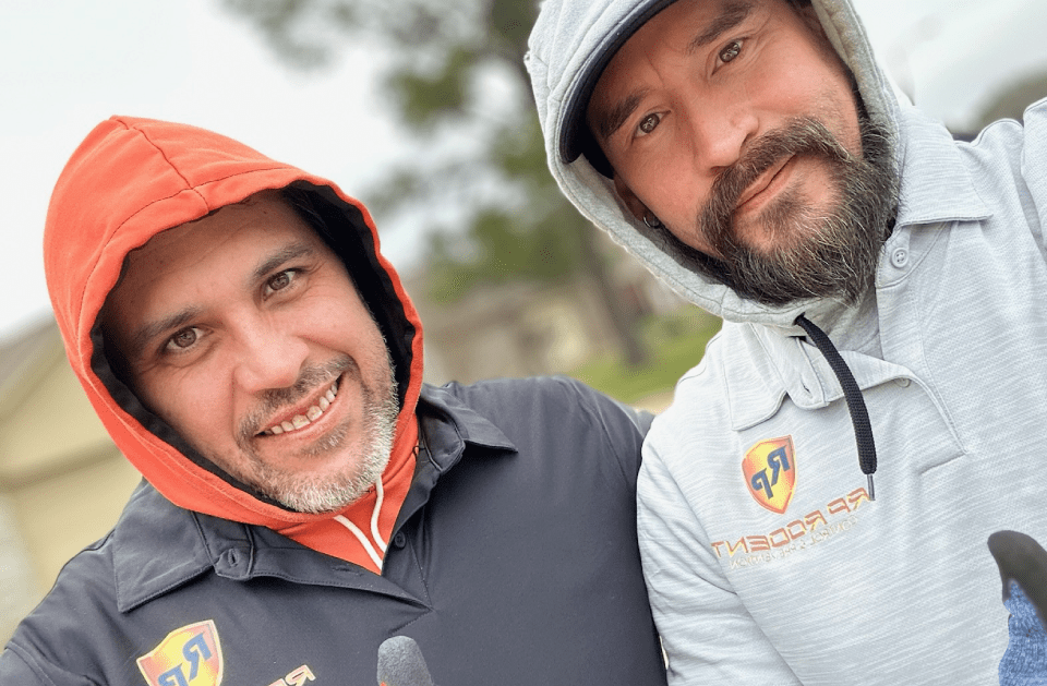 Two men in hoodies smiling outdoors. One in orange, one in gray with logo.
