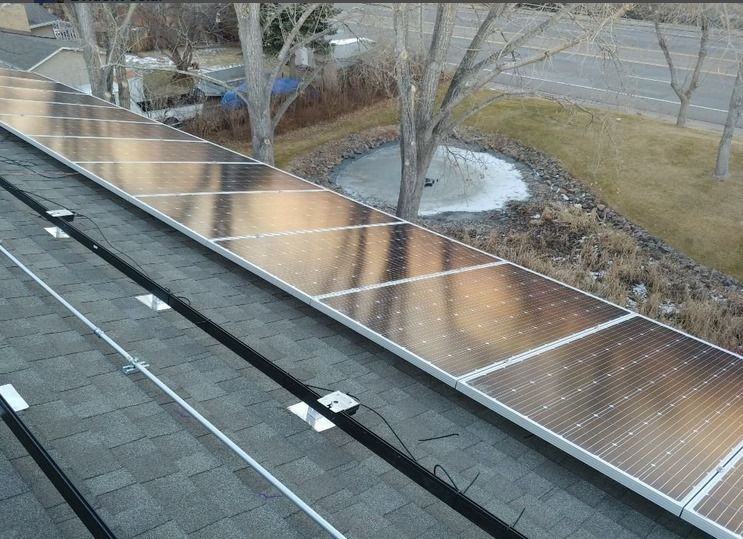 A row of solar panels on a roof with trees in the background.