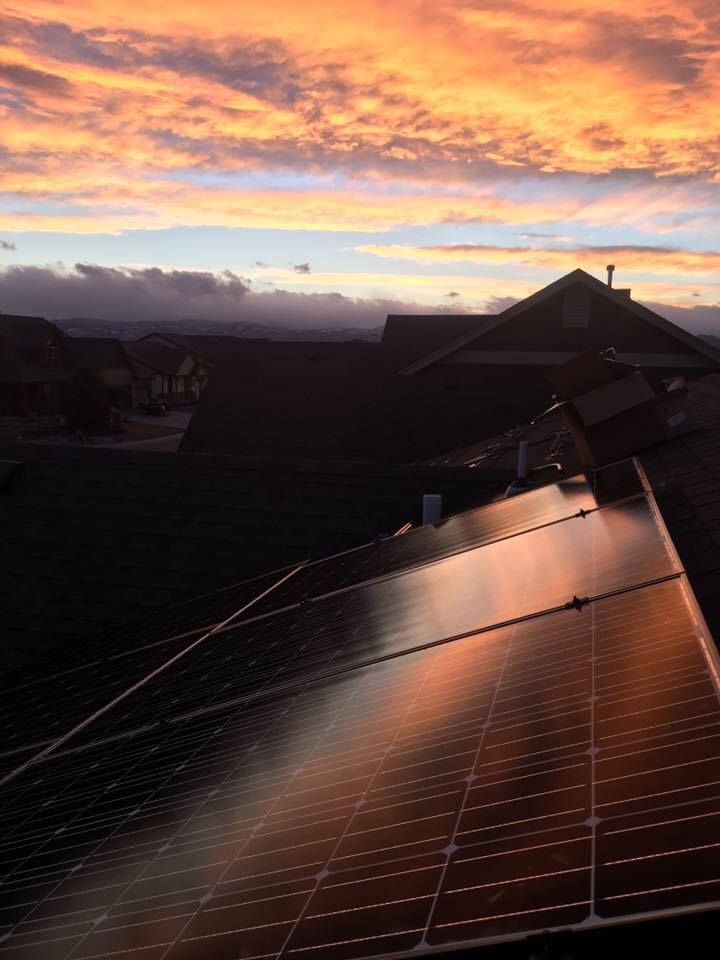 A row of solar panels on the roof of a house at sunset.