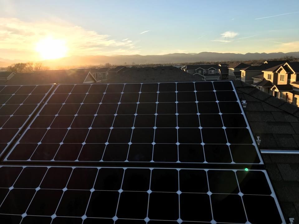 The sun is setting behind the solar panels on the roof