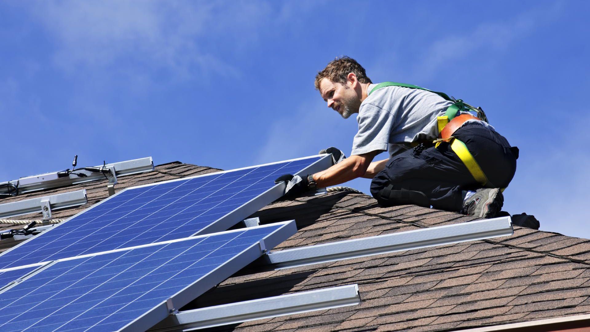 A man is installing solar panels on the roof of a house.