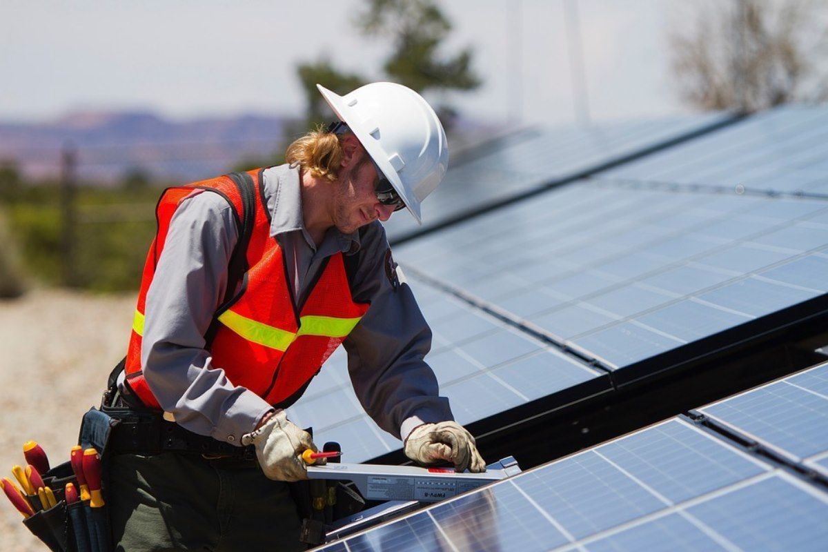 A man wearing a hard hat is working on a solar panel.