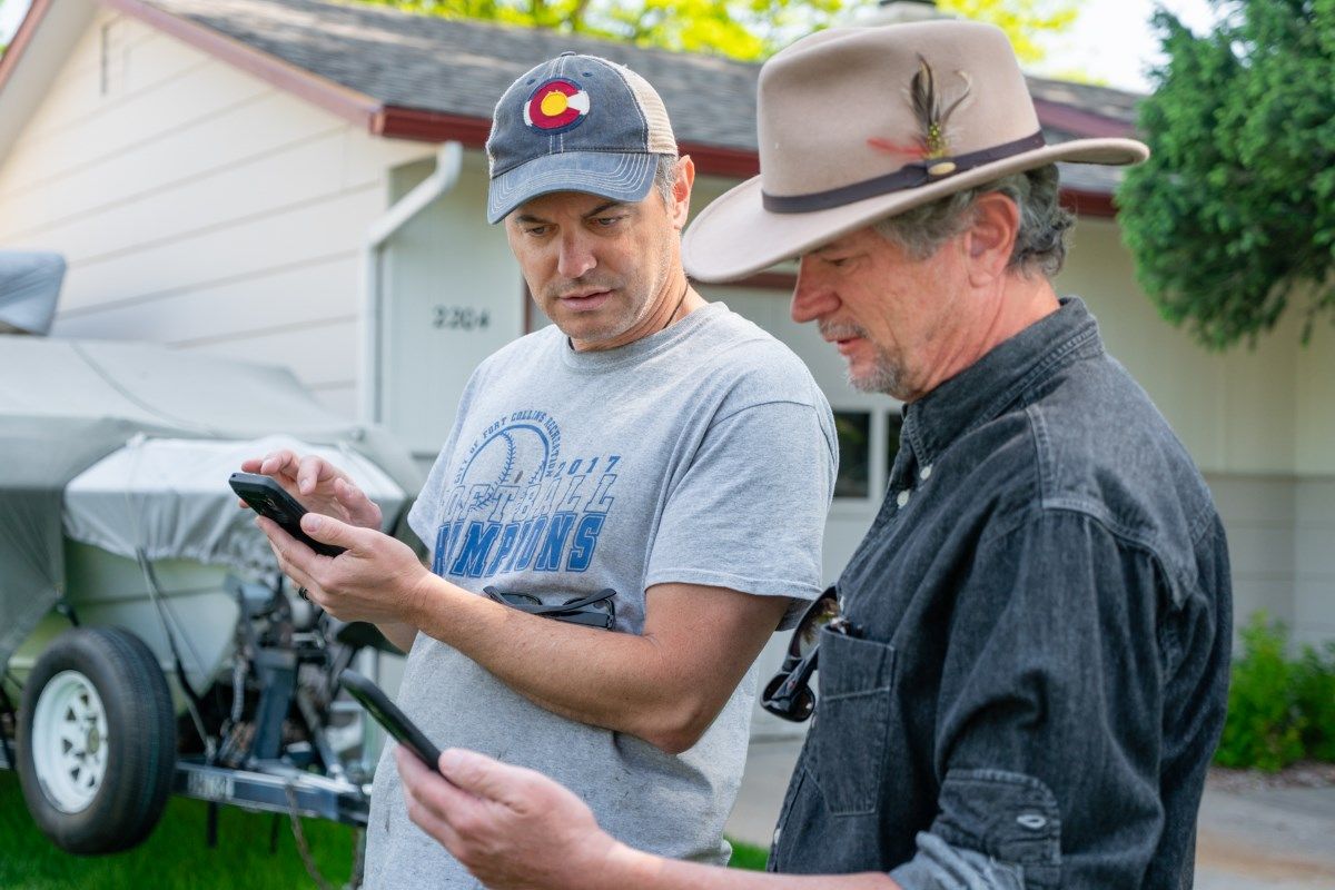 Two men are looking at a cell phone in front of a house.