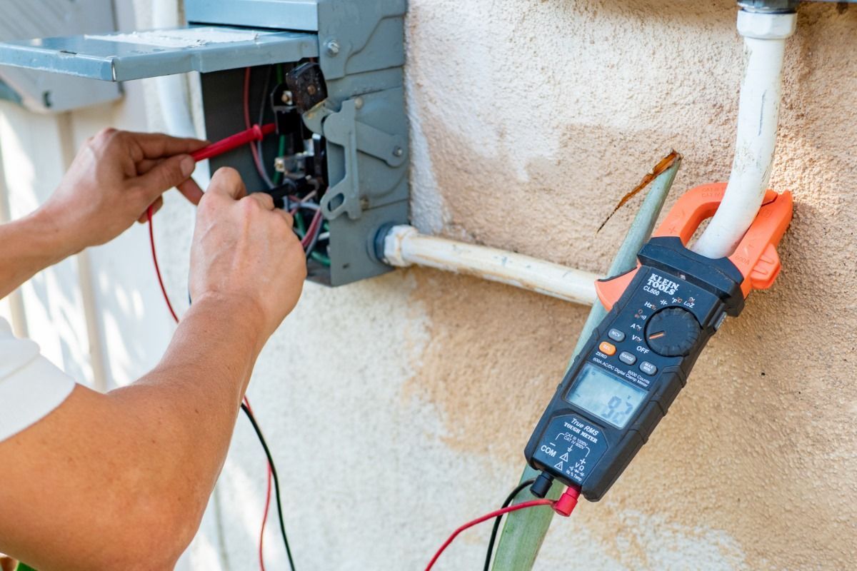 A person is using a clamp meter to test an electrical box.