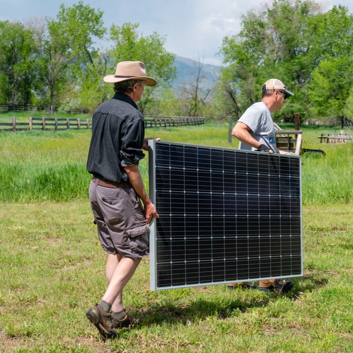Two men are carrying a solar panel in a field.