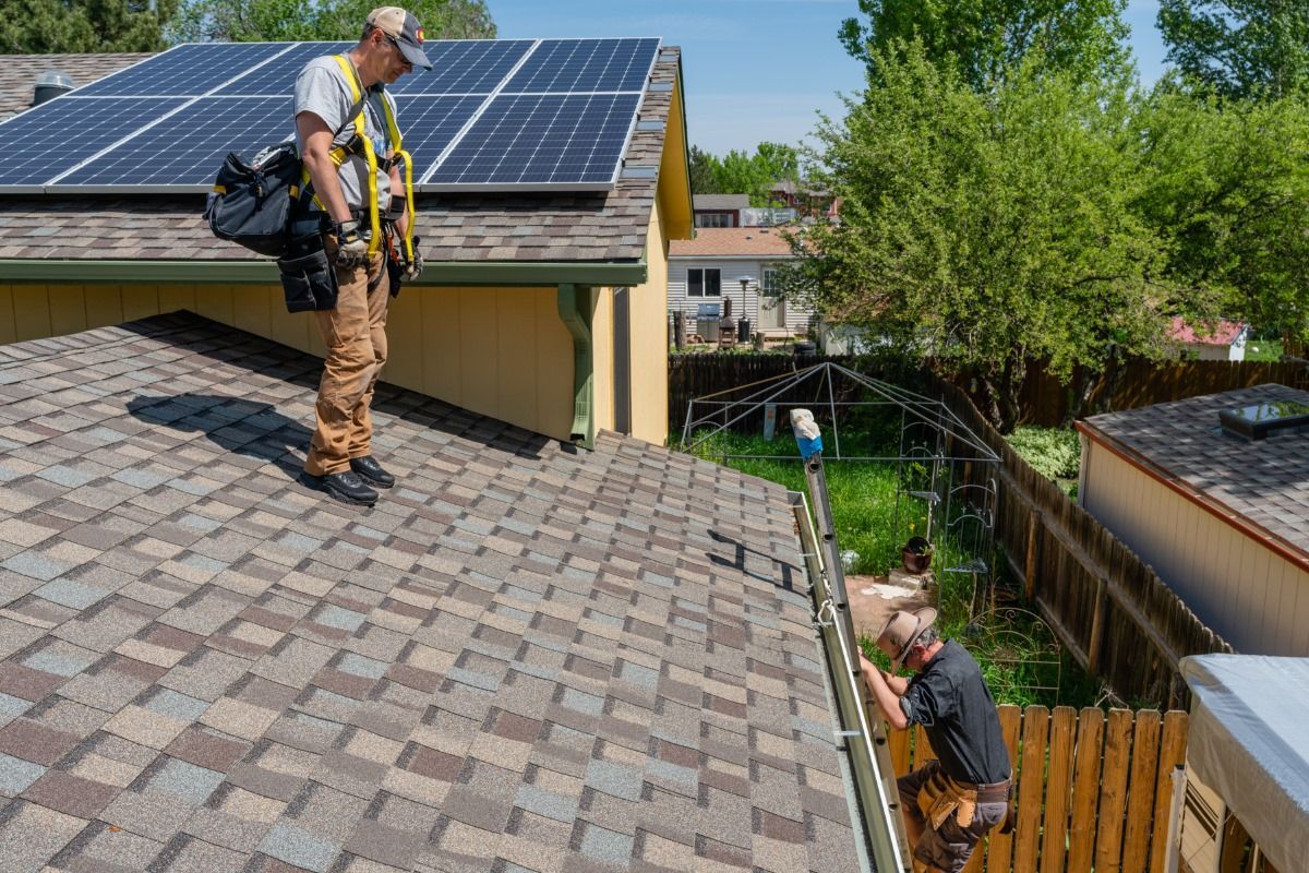 Two men are working on the roof of a house with solar panels.