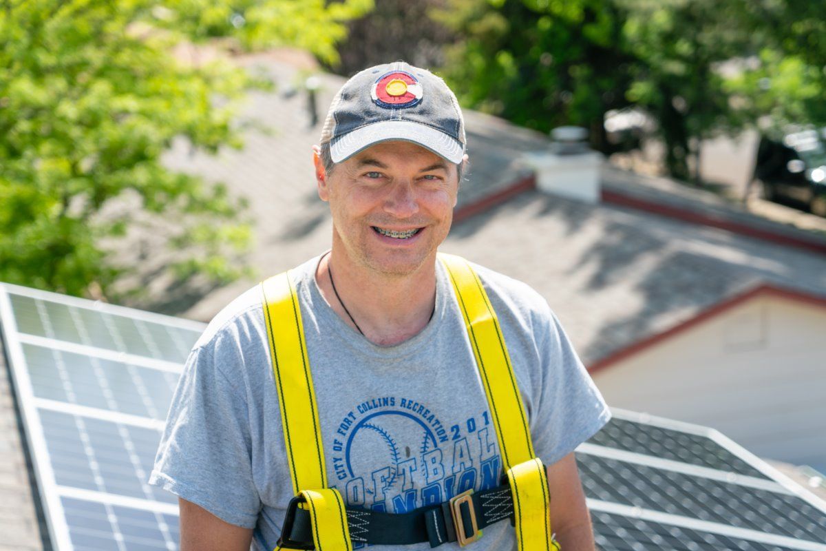 A man is standing on top of a roof with solar panels.