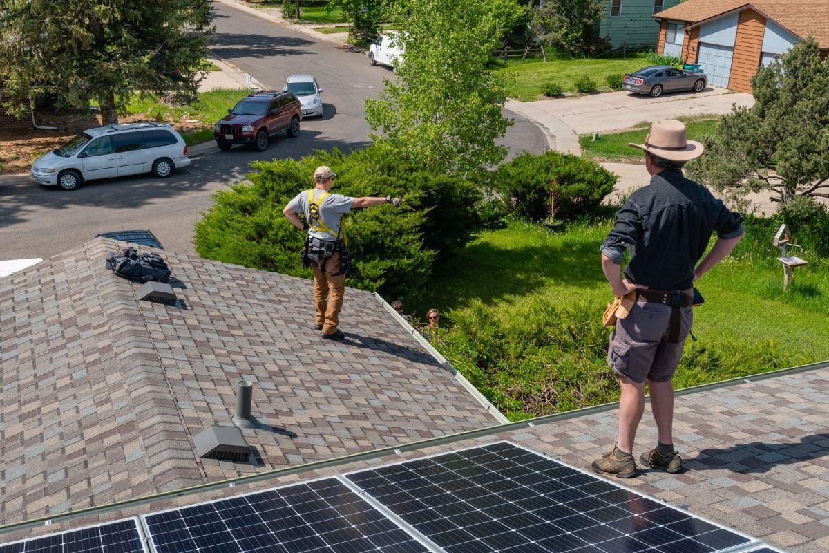 Two men are standing on top of a roof with solar panels.