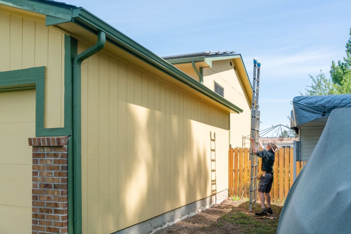 A man is working on the side of a yellow house.