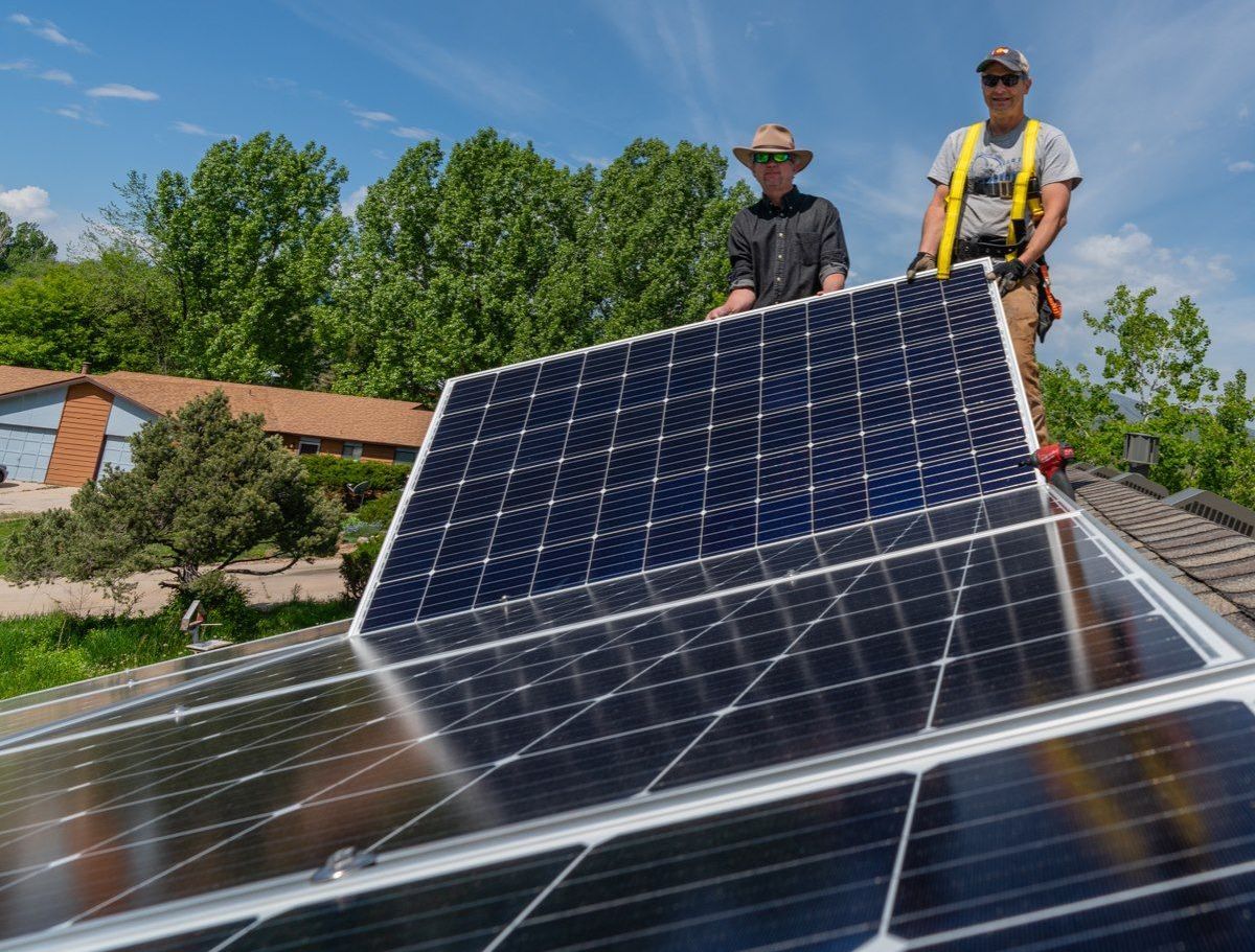 Two men are installing solar panels on the roof of a house.