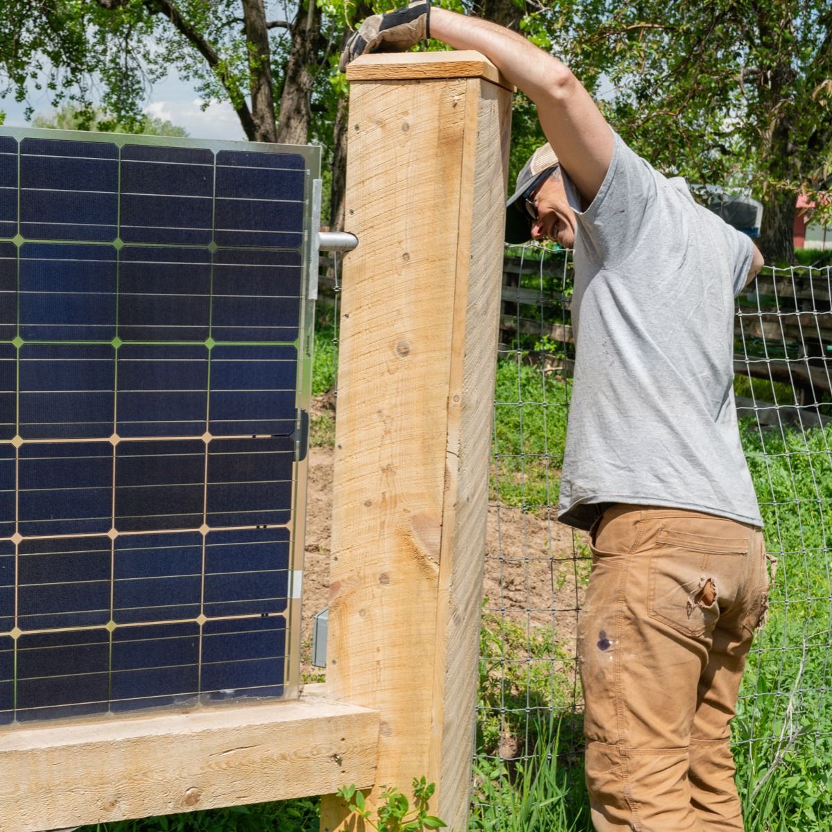 A man is standing next to a solar panel on a wooden post