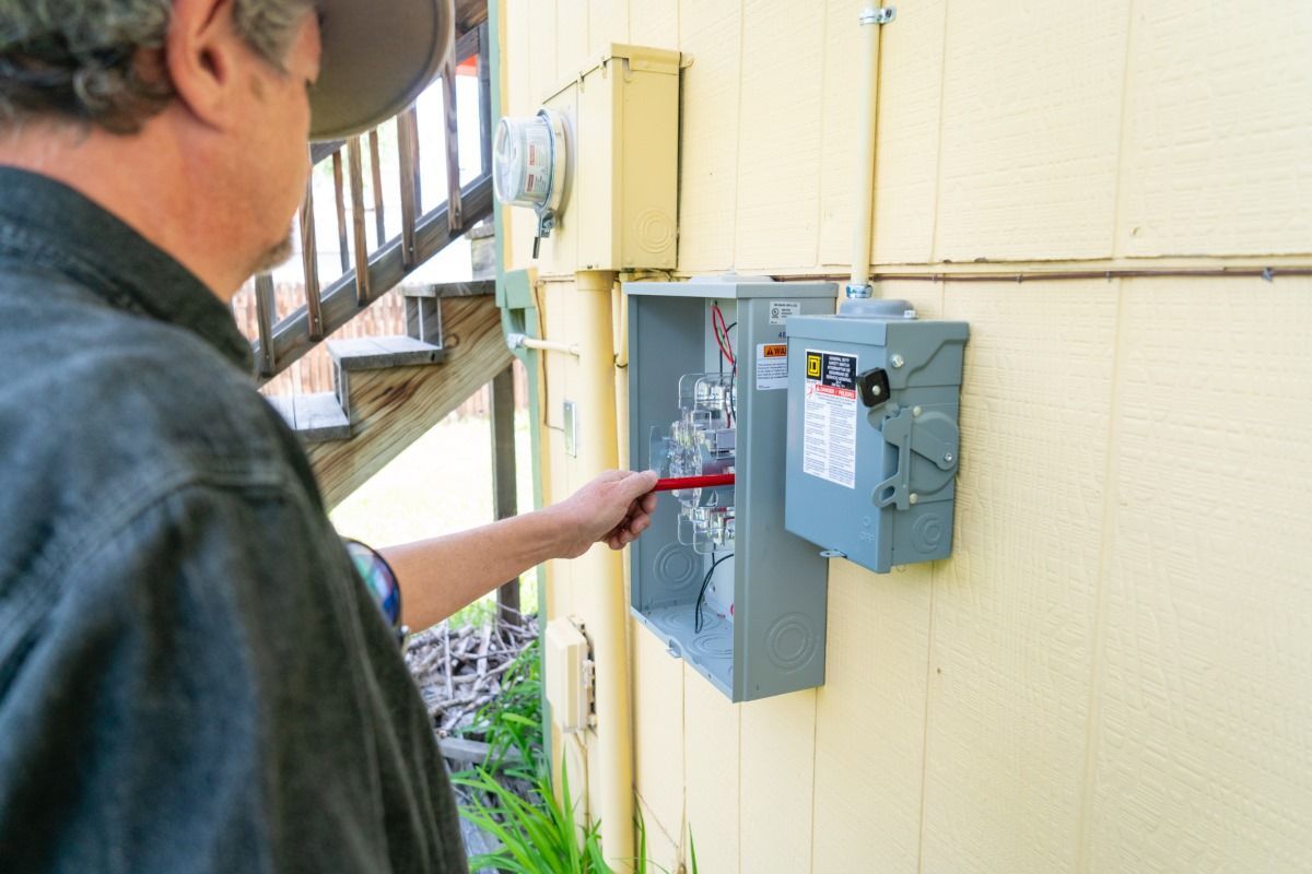 A man is pointing at an electrical box on the side of a building.