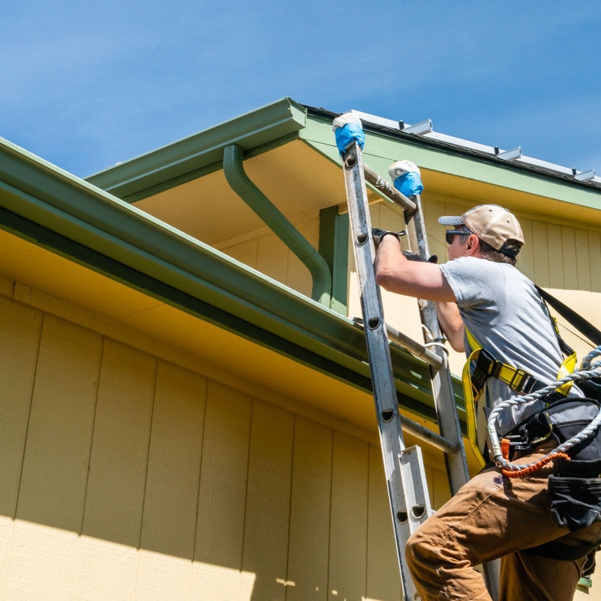 A man is climbing a ladder to fix a gutter on a house