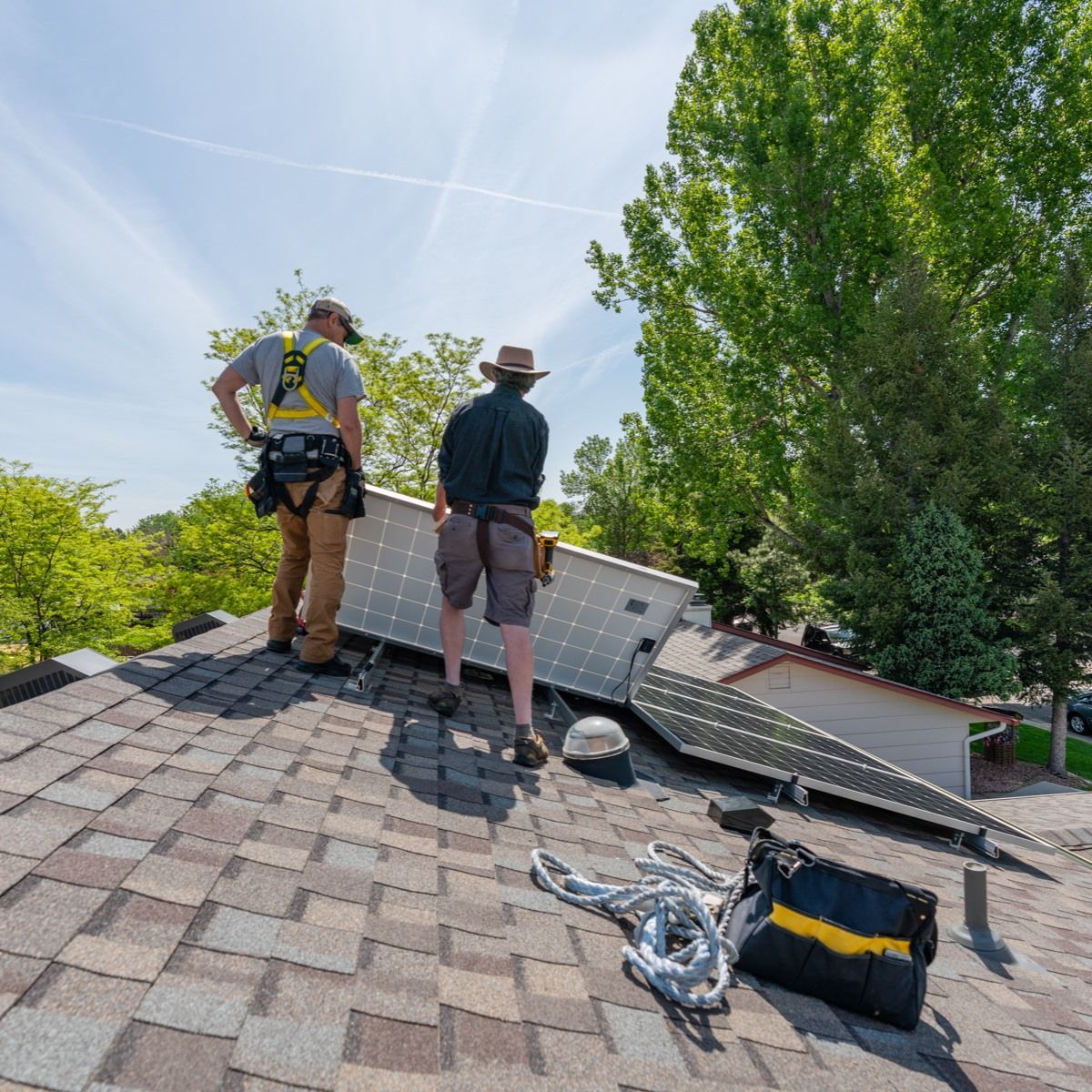 Two men are standing on top of a roof looking at a solar panel.