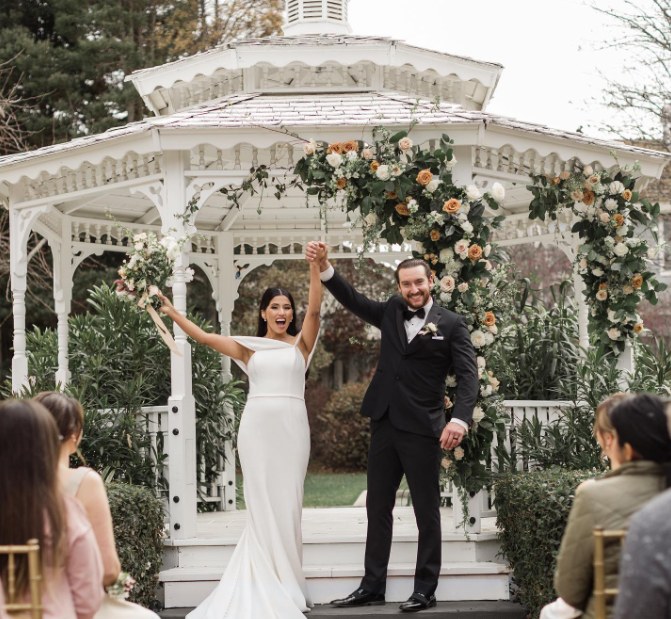 A bride and groom are holding hands in front of a gazebo
