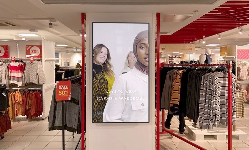 There is a large screen in the middle of a clothing store.