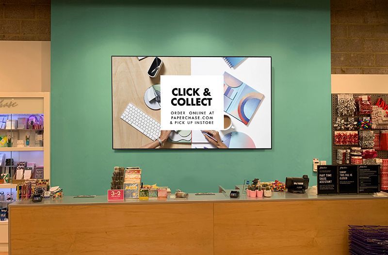 A large flat screen tv is hanging on a wall above a counter in a store.