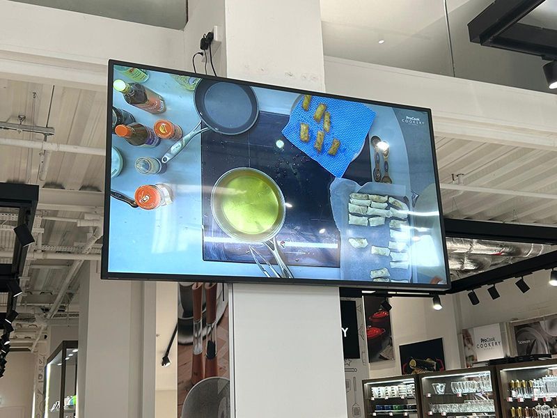 A large flat screen tv is hanging from the ceiling in a kitchen