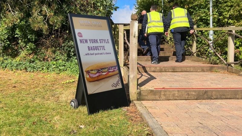 Two men are walking down stairs next to a sign that says new york style baguette.
