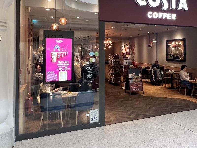 A costa coffee store with people sitting at tables in front of it.