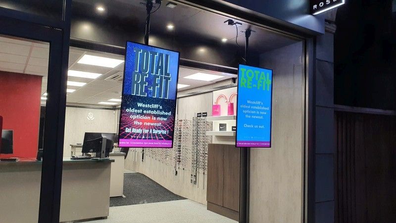 A store front with two digital signs hanging from the ceiling.