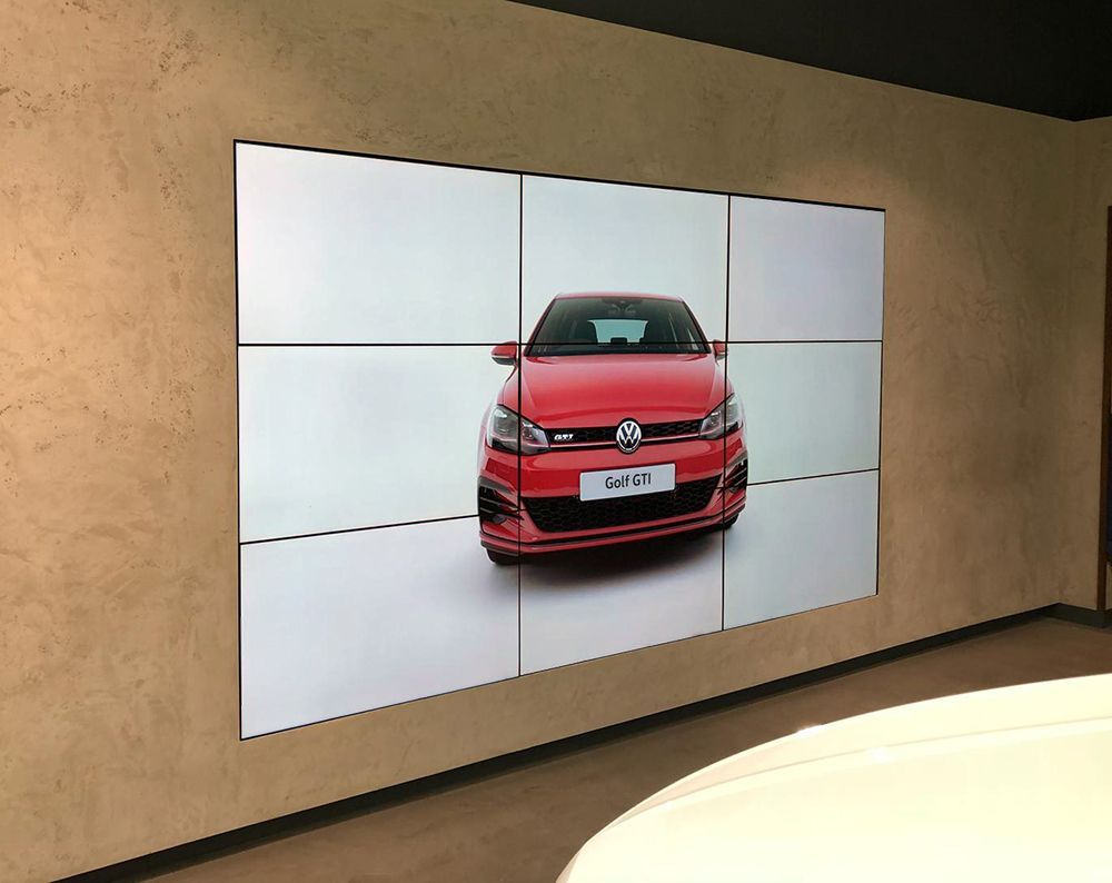 A large screen displays a picture of a red volkswagen golf on a wall.