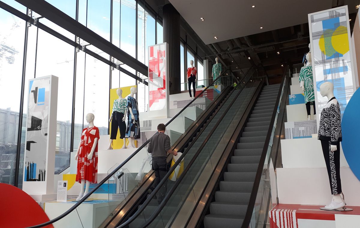 A man is riding an escalator in a store surrounded by mannequins.