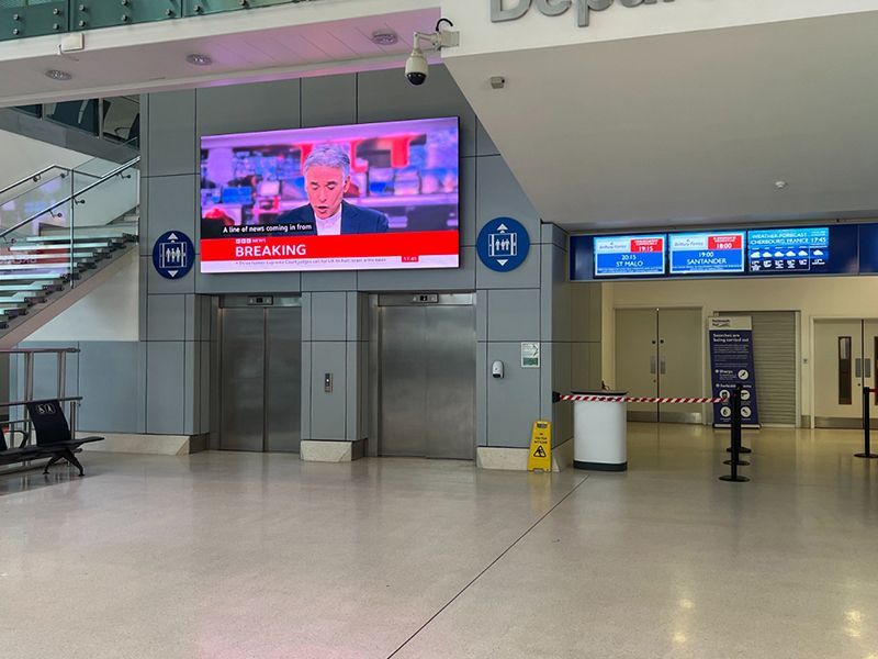 A large screen is hanging from the ceiling of an airport