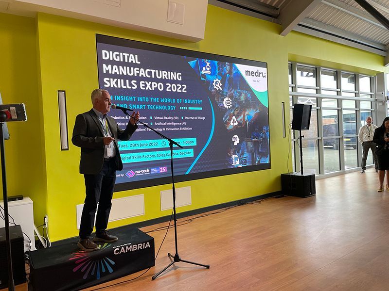 A man is standing on a stage in front of a large screen that says digital manufacturing skills expo 2022.