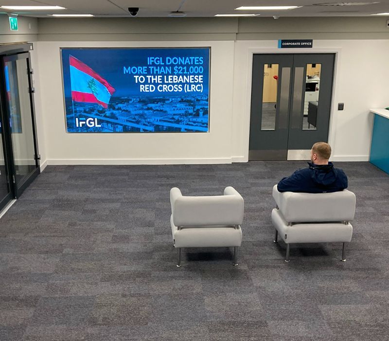 A man sits in a chair in front of a sign that says ifgl donates more than $ 25,000 to the lebanese red cross