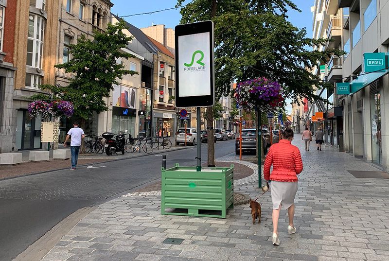 A woman in a red jacket is walking down a sidewalk with a dog.