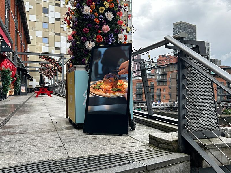 A sign on a sidewalk with a picture of a pizza on it.