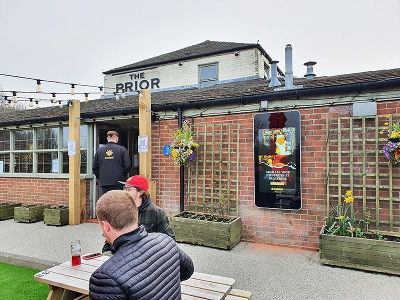 A group of people are sitting at a picnic table outside of a restaurant.