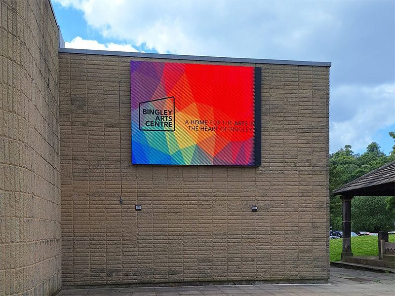 A large colorful sign is hanging on the side of a brick building.