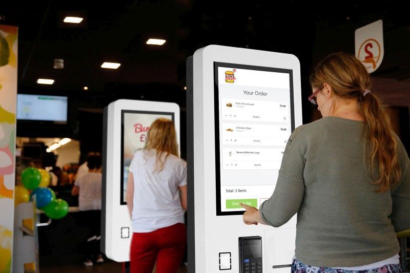 A woman is using a kiosk at a fast food restaurant.