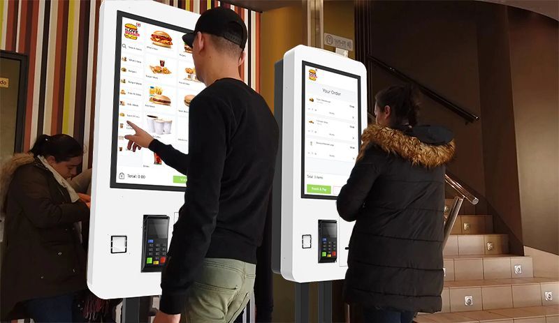A man is pointing at a screen in a fast food restaurant.
