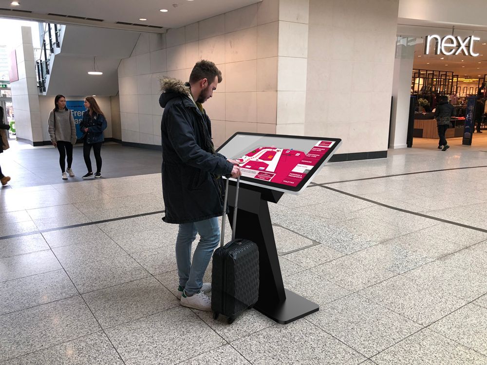A man with a suitcase is standing in front of a large screen.