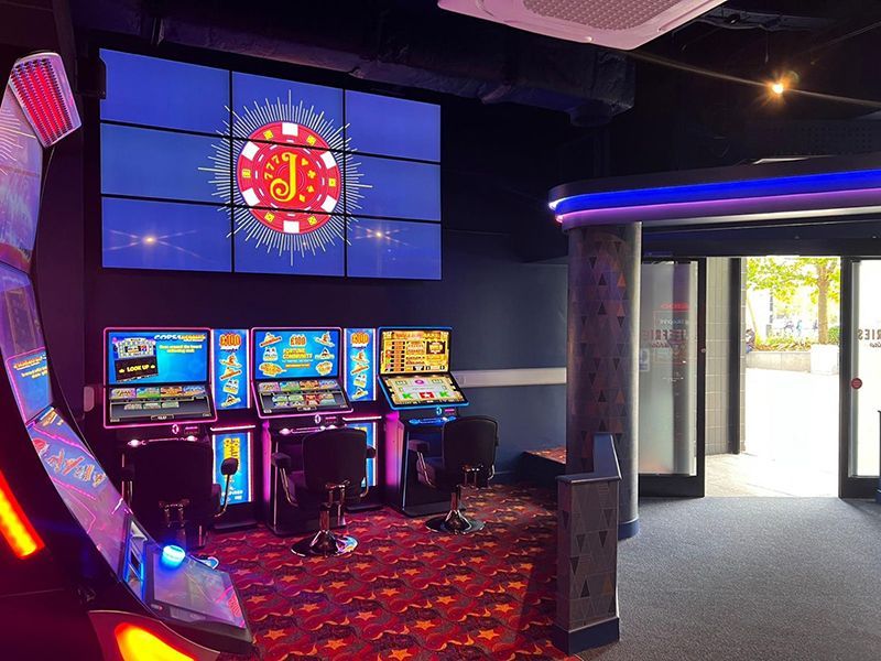 A casino with a lot of slot machines and a large screen on the wall.