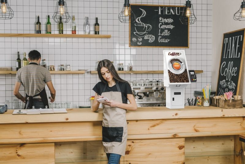 A woman is standing at a counter in a coffee shop looking at her phone.