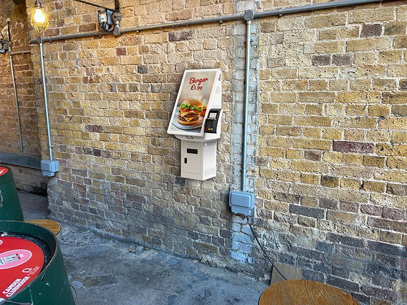 A brick wall with a burger machine on it.